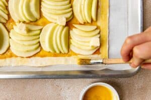 a pastry brush brushing egg wash on puff pastry dough.