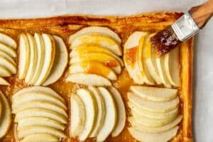 a brush brushing on apricot preserves on an apple tart.