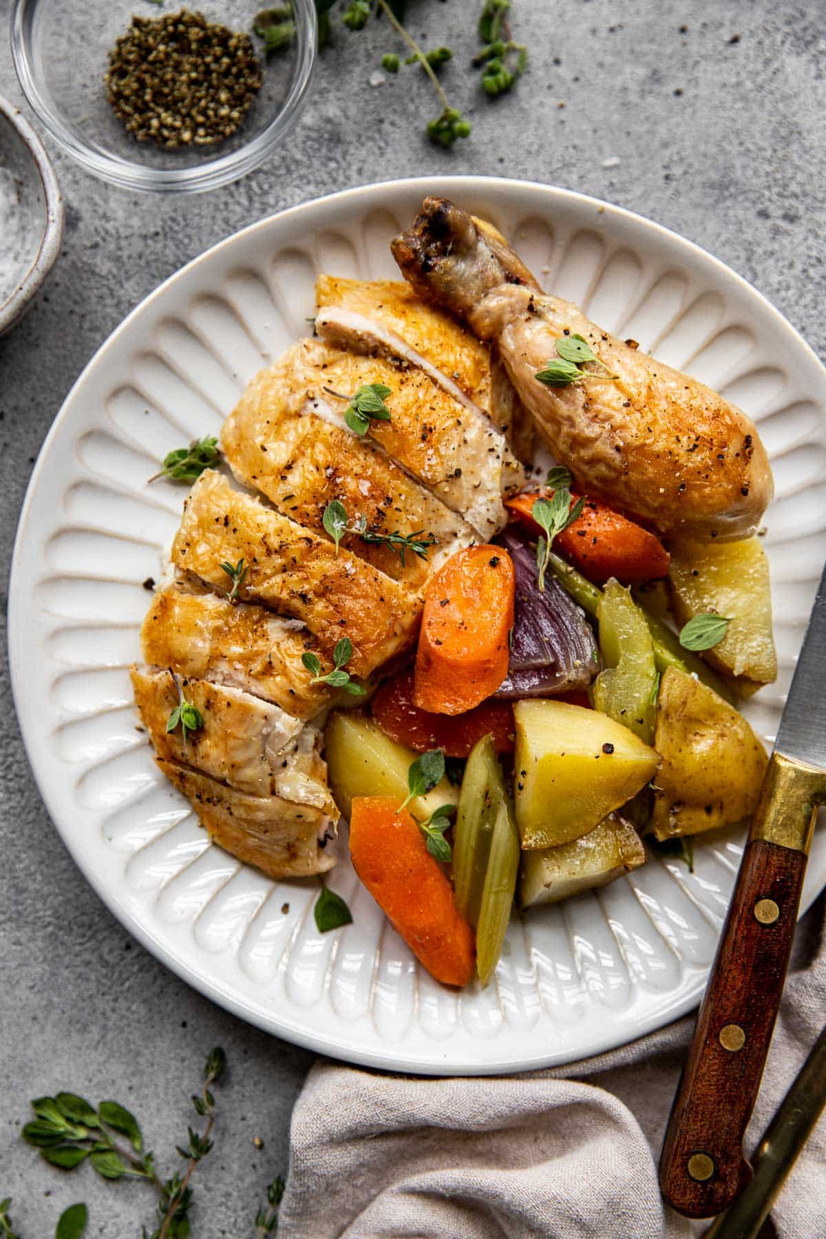 carved and cut chicken on a white plate with veggies and potatoes. 