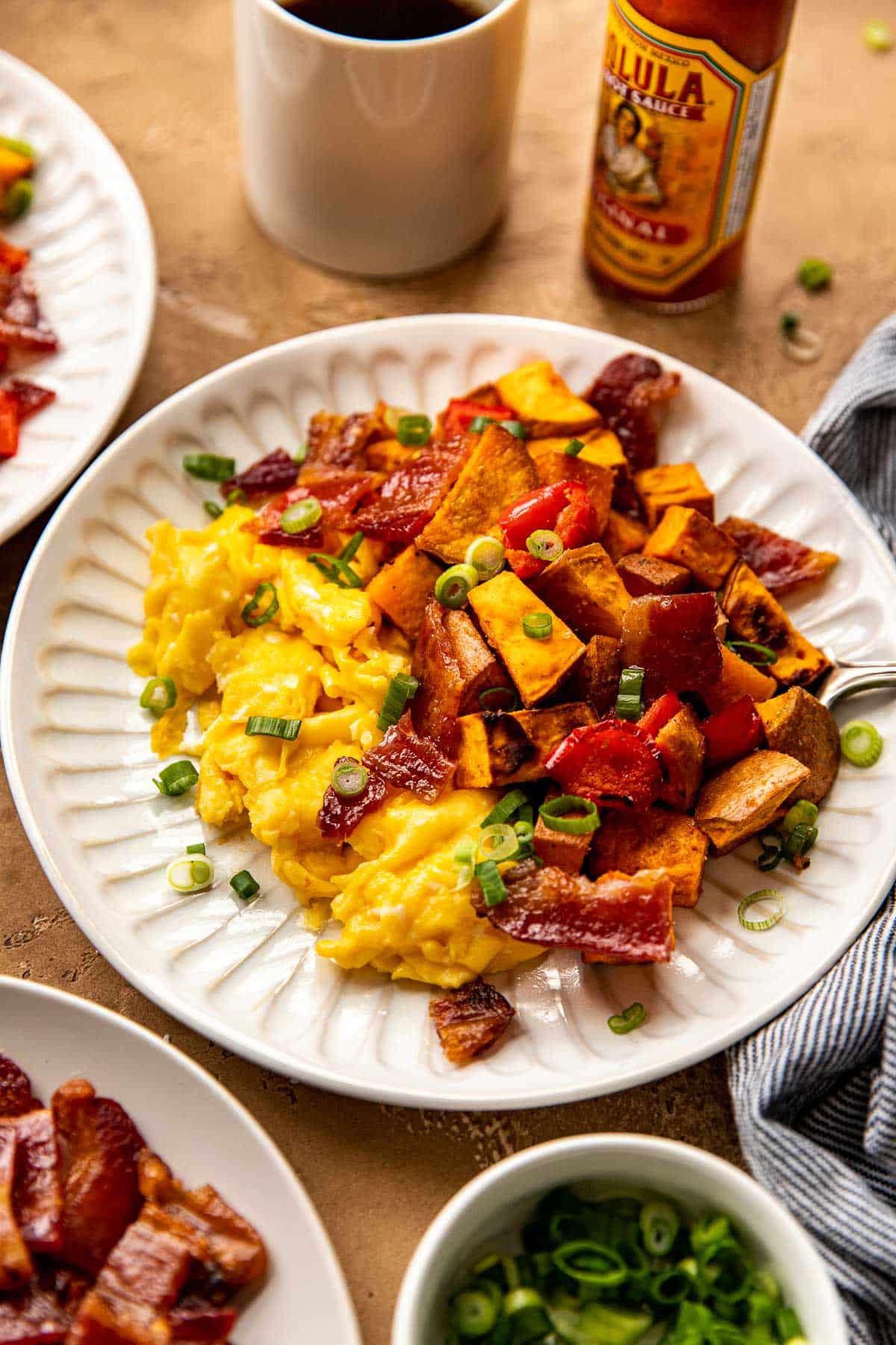scrambled eggs, sweet potatoes, candied bacon on a white plate garnished with green onions. 