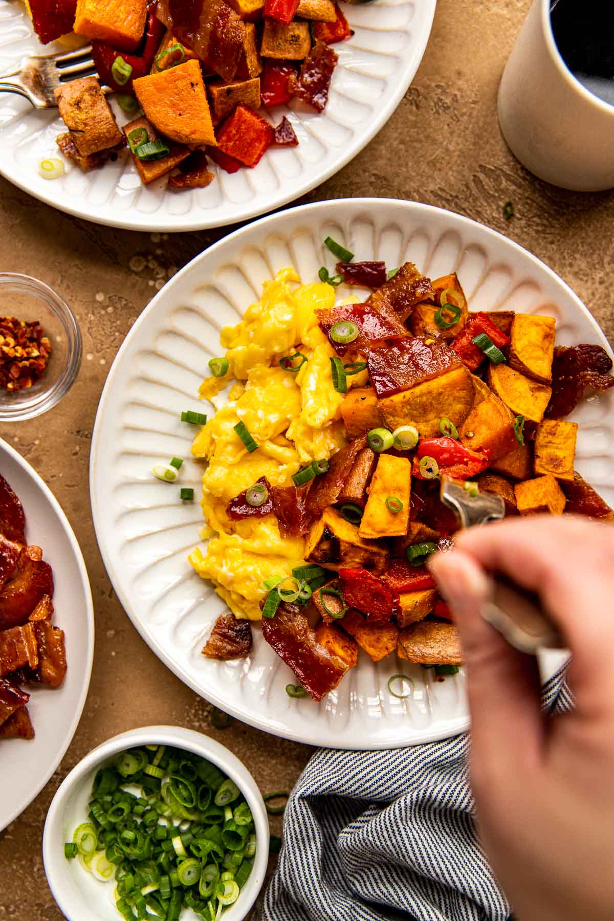 scrambled eggs, sweet potatoes, candied bacon on a white plate garnished with green onions. 