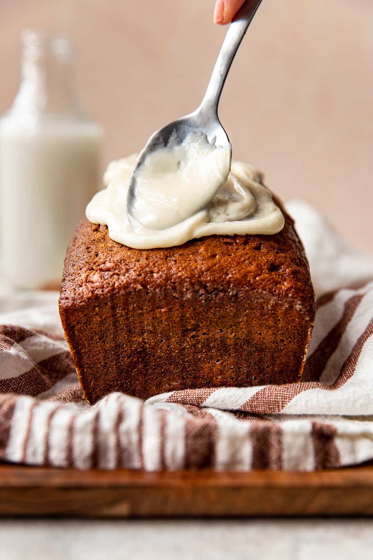 frosting being spread on a banana bread with a spoon.