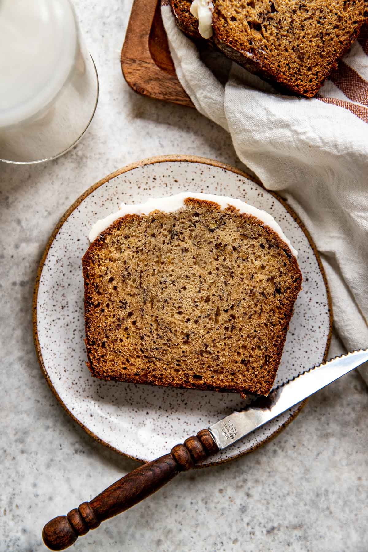 a slice of banana bread on a white speckled plate with a knife on the side of the plate. 