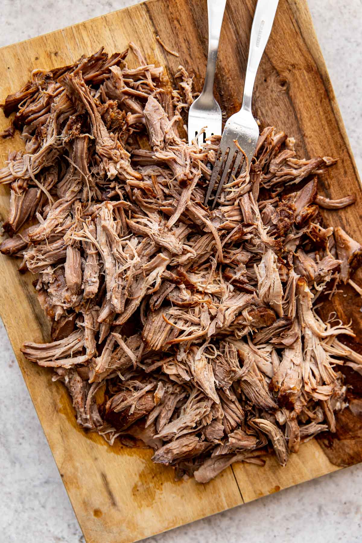 pulled pork shredded with forks on a cutting board. 