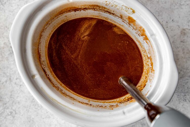 an immersion blender blending the sauce in a white crock pot.