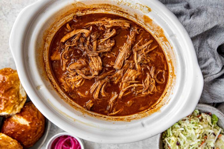 pulled pork mixed in the sauce in a white crock pot.