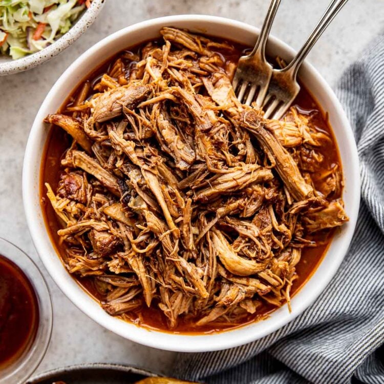 pulled pork in a white bowl with two forks.