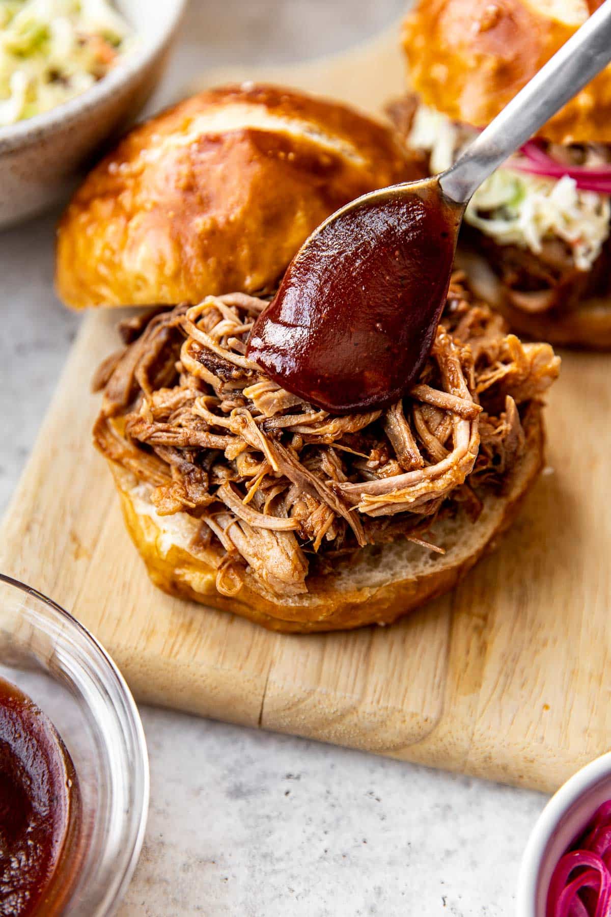 pulled pork on a pretzel bun with bbq sauce being spooned on top of the pork. 