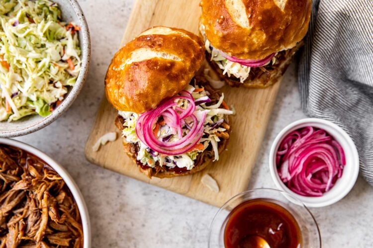 a sandwich made from pulled pork on a cutting board with coleslaw and pickled red onions.