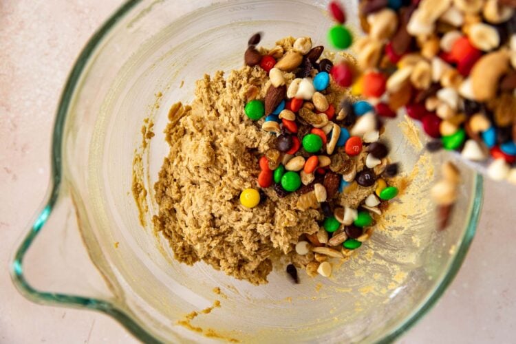 trail mix being poured into cookie dough for trail mix cookies.