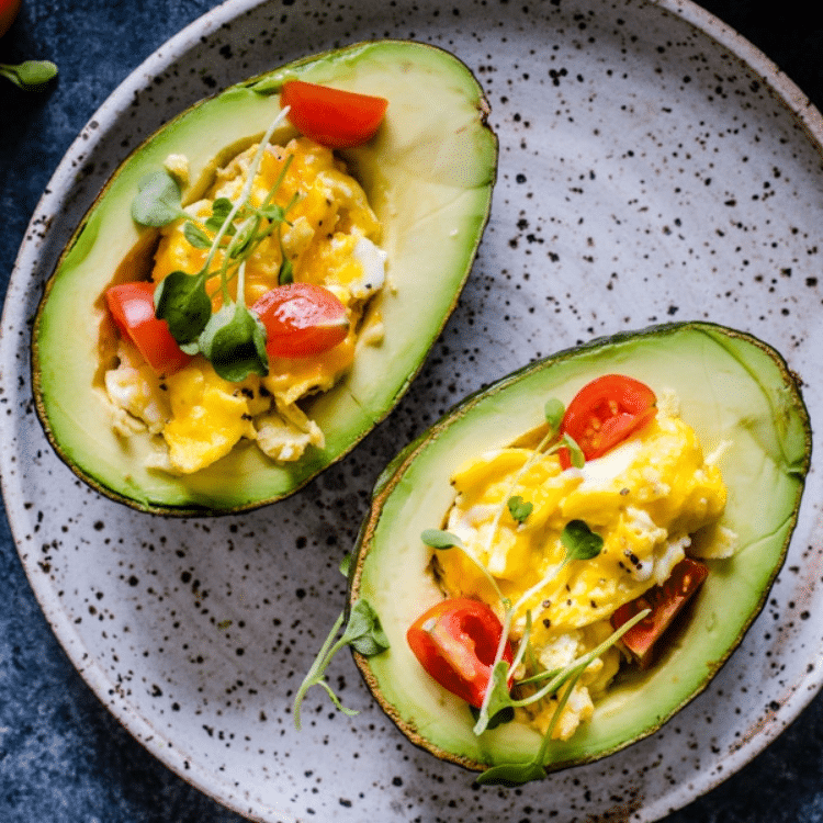 two halves of an avocado stuffed with scrambled eggs and tomatoes