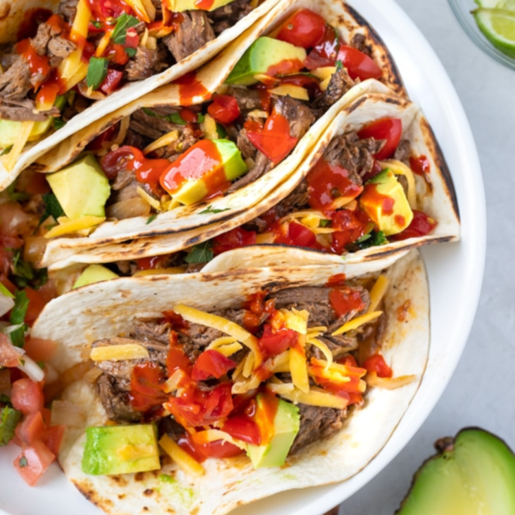 tacos with beef, avocado, and sauce in a white bowl