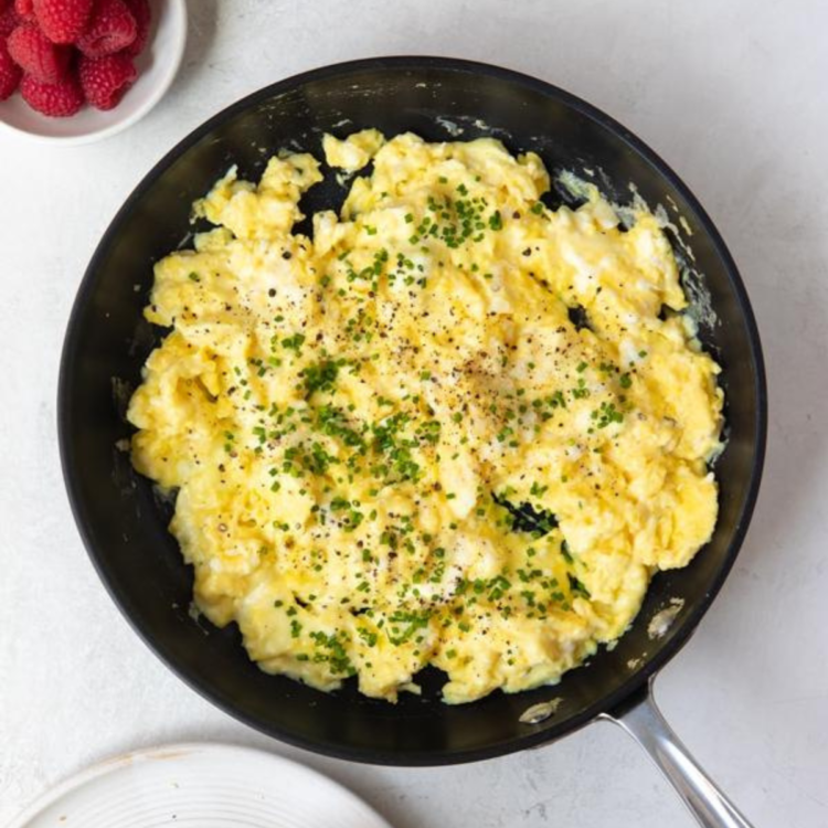 black skillet with scrambled eggs topped with chives