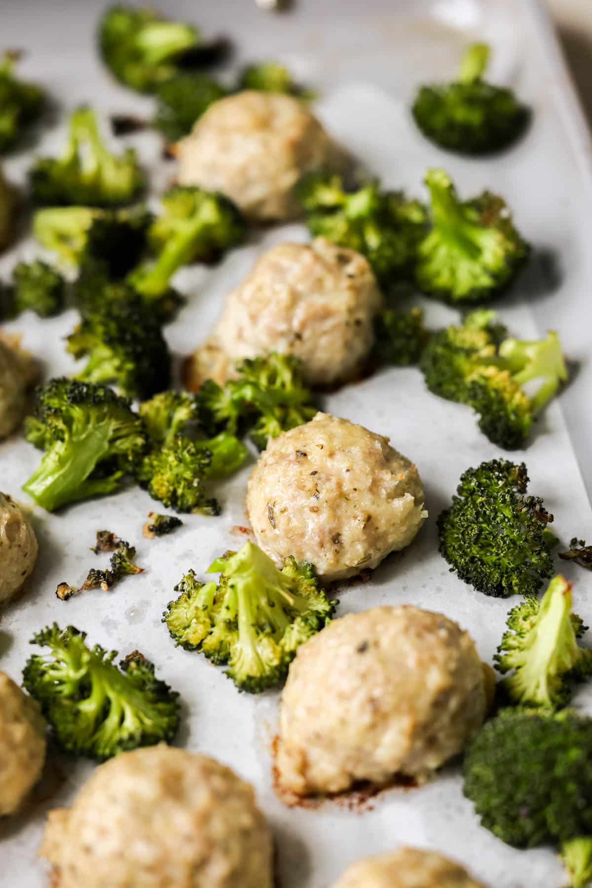 cooked chicken meatballs and roasted broccoli on a sheet pan. 