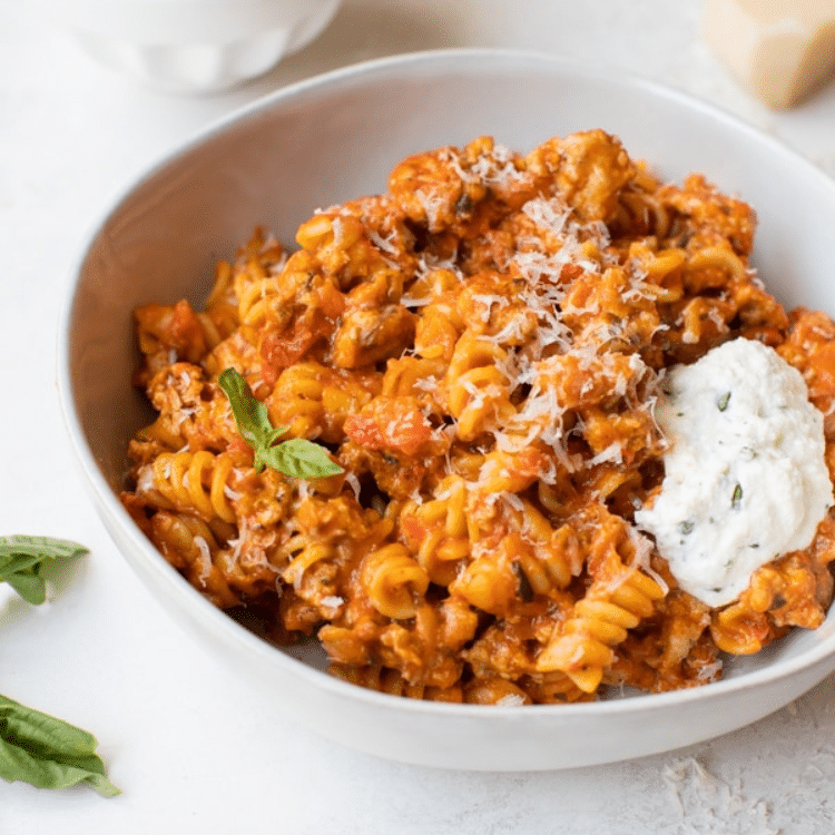 white bowl with rotini pasta in red sauce with scoop of creamy white cheese