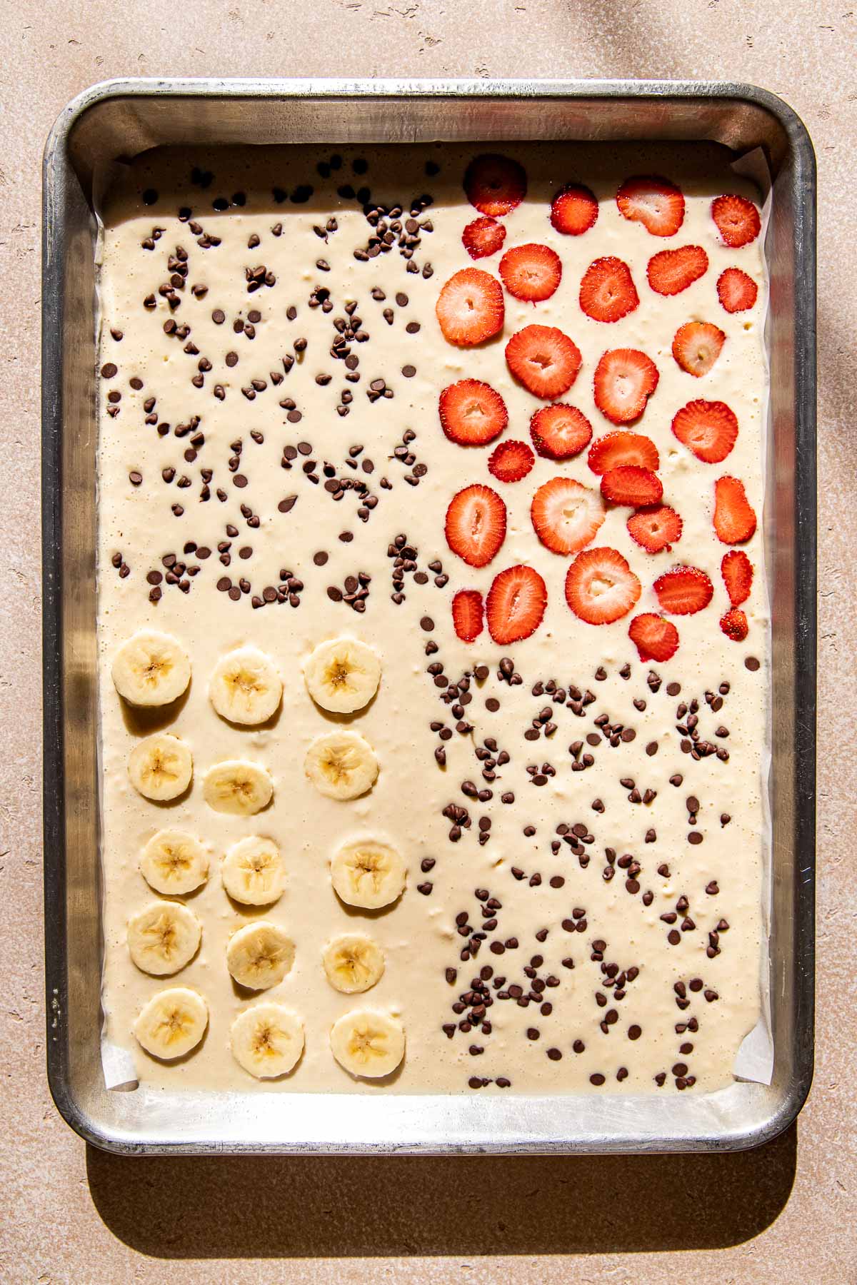 pancake batter on a sheet pan with fresh fruit and chocolate chips.