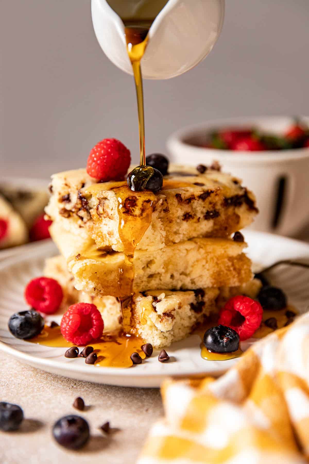 pancakes on a white plate with fresh berries and syrup poured on top. 