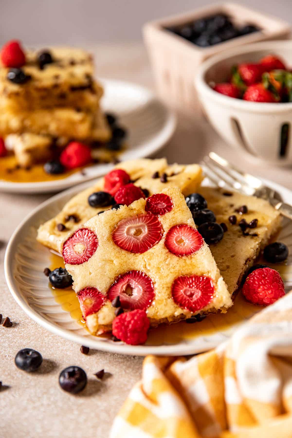 pancakes on a white plate with fresh berries and syrup poured on top. 
