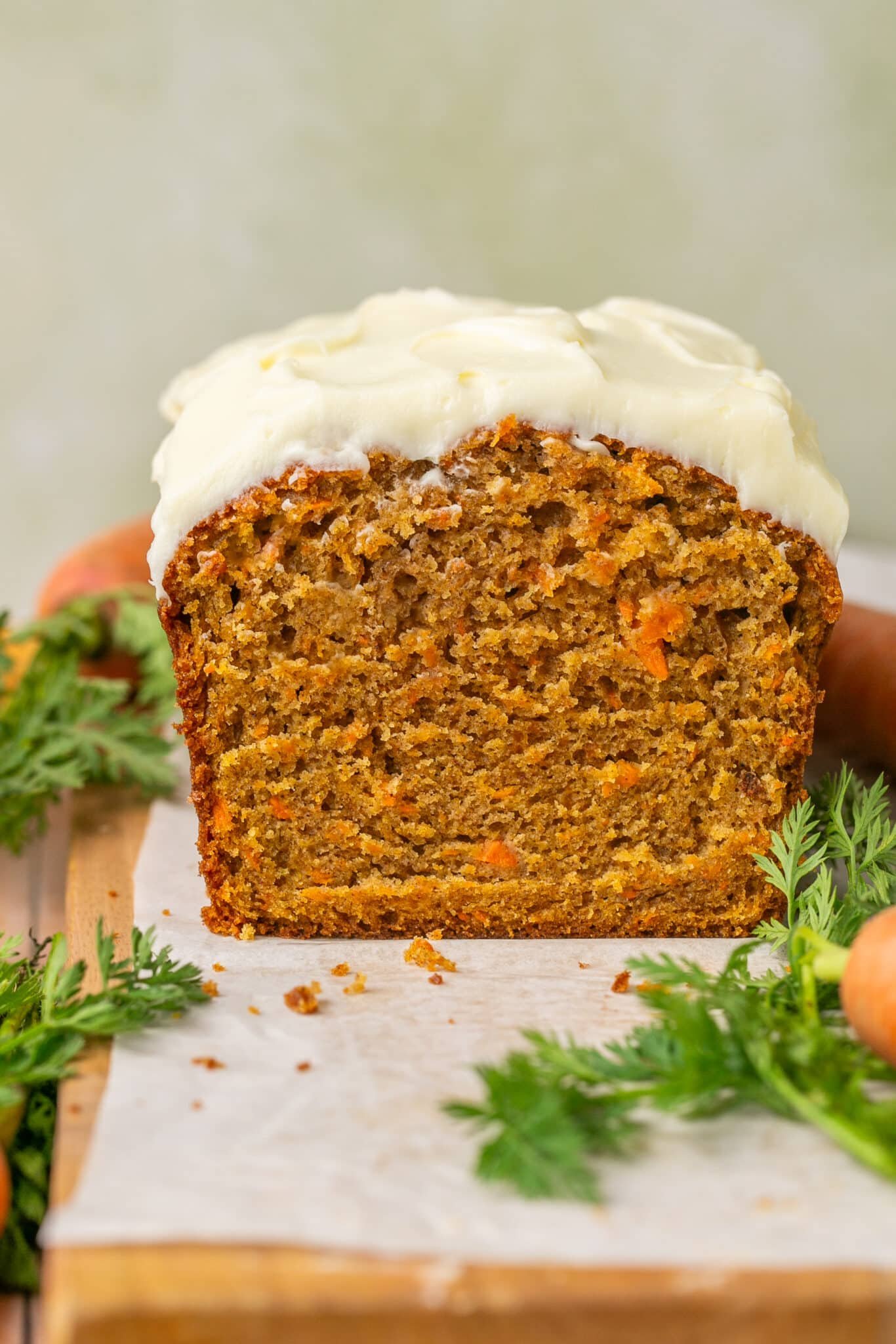 a loaf of carrot cake on a cutting board lined with parchment paper. 