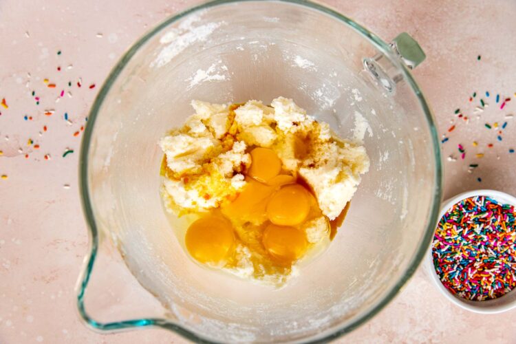eggs and vanilla extract in a glass mixing bowl with creamed butter and sugar.