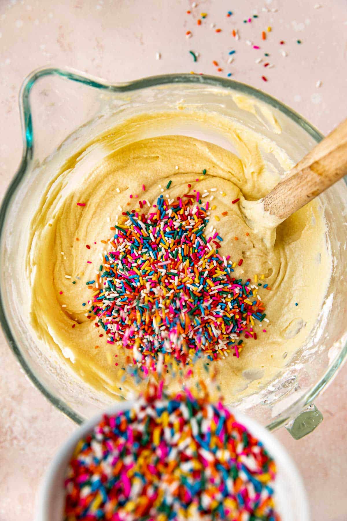 sprinkles being poured into cake batter in a glass mixing bowl. 
