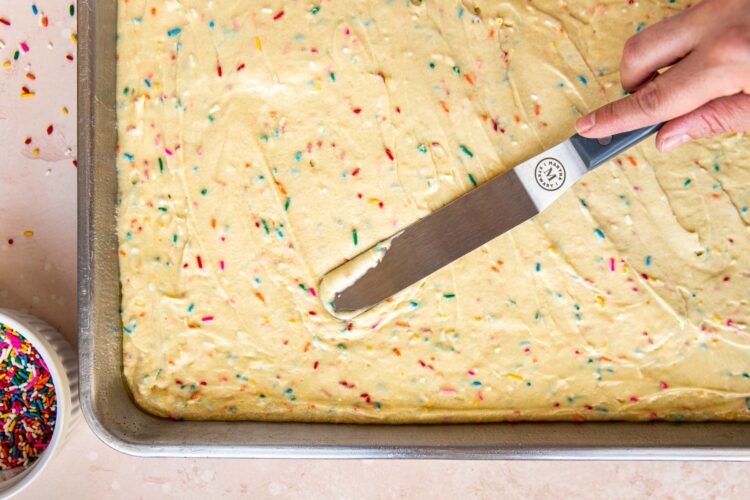 an offset spatula spreading cake onto a sheet pan.