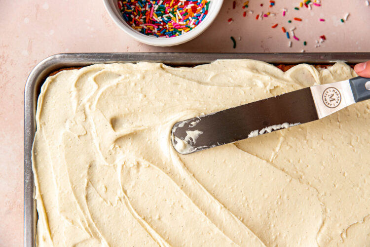 frosting being spread on top of a funfetti cake with an offset spatula.