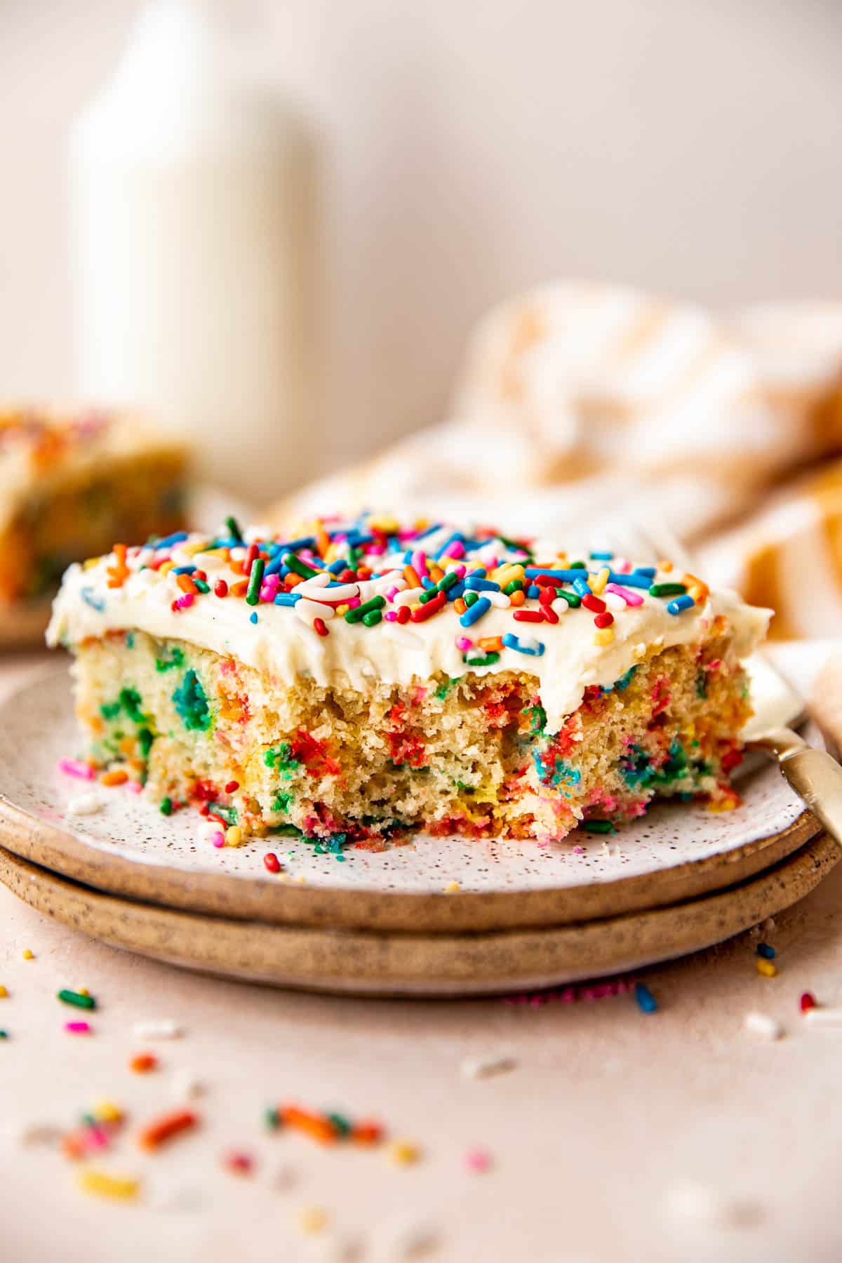 funfetti cake on a plate with a bite taken out of it. 