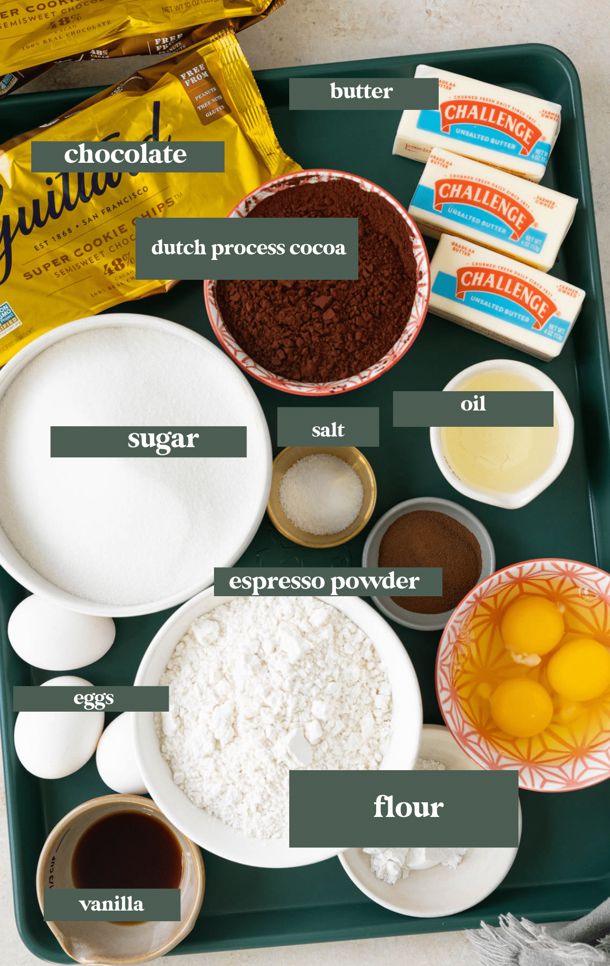 ingredients to make brownies in small glass bowls laid out on a green sheet pan. 