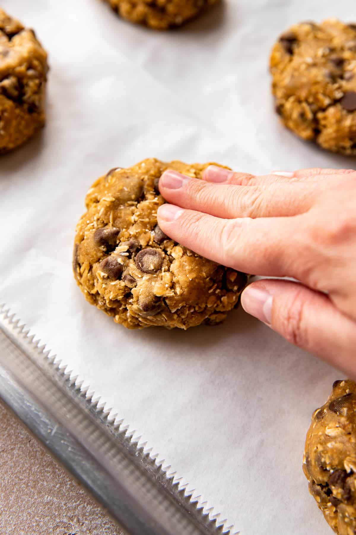 a hand pressing down cookie down on a sheet pan lined with parchment. 