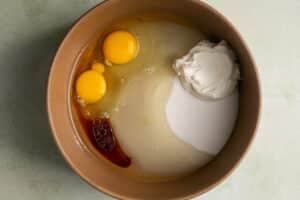 sugar, eggs, oil, vanilla, and sour cream in a wooden mixing bowl.