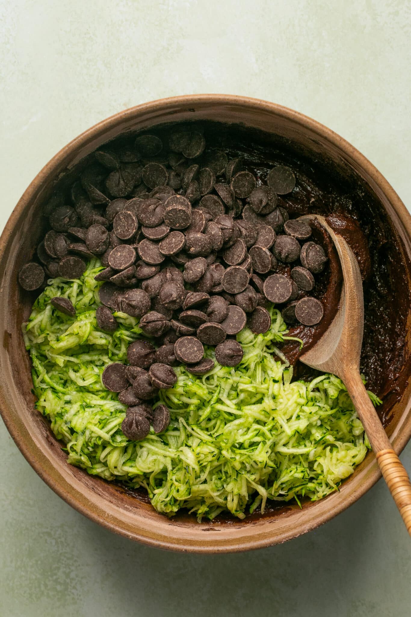 a wooden bowl with chocolate zucchini bread batter with grated zucchini and dark chocolate chips. 