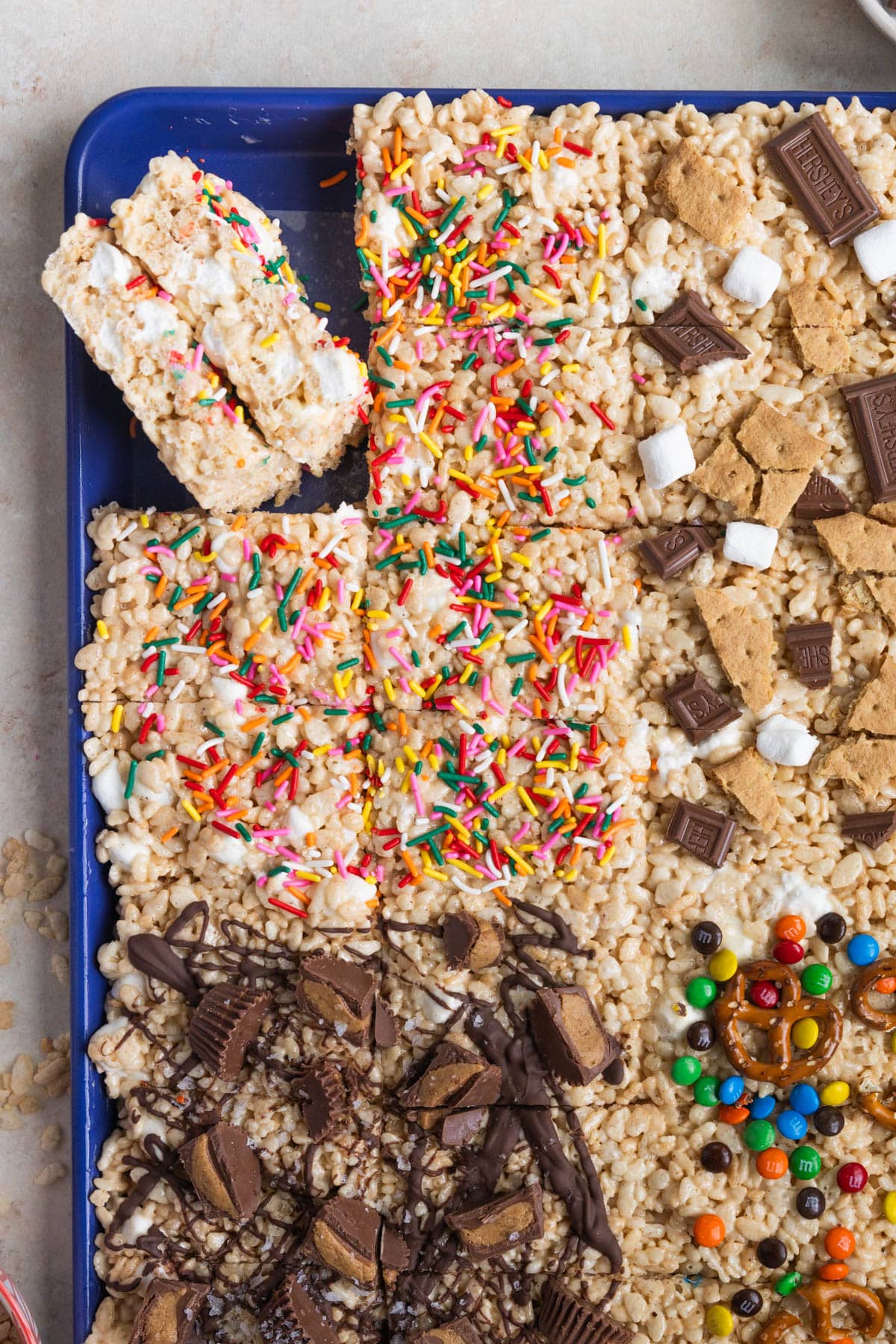 rice krispies treats on a blue sheet pan with different toppings. 