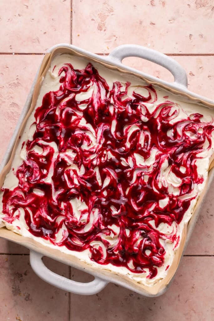 no bake cheesecake in a pan with berry sauce swirled on top.