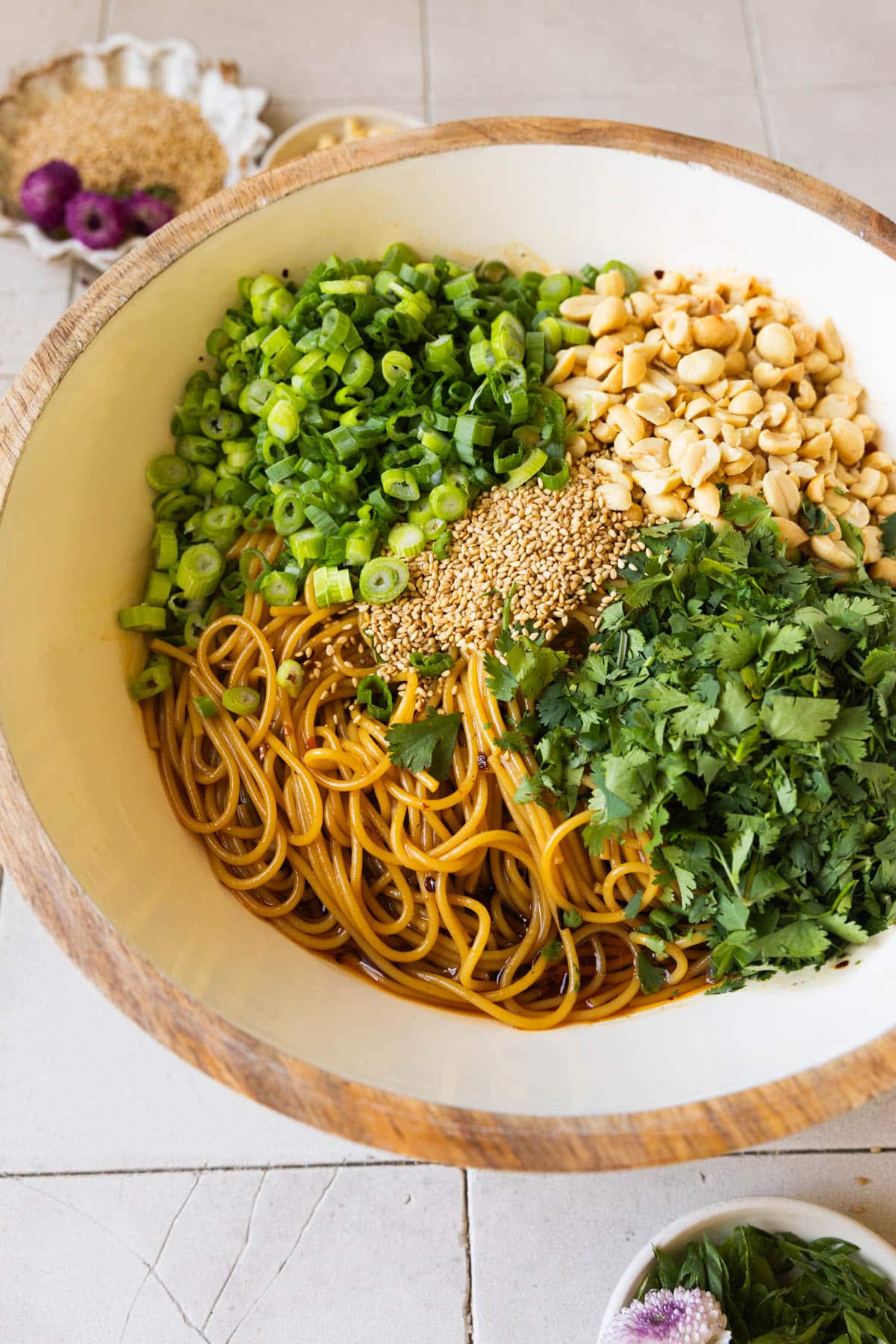 spicy noodles in a white bowl with green onions, peanuts, sesame seeds and cilantro. 