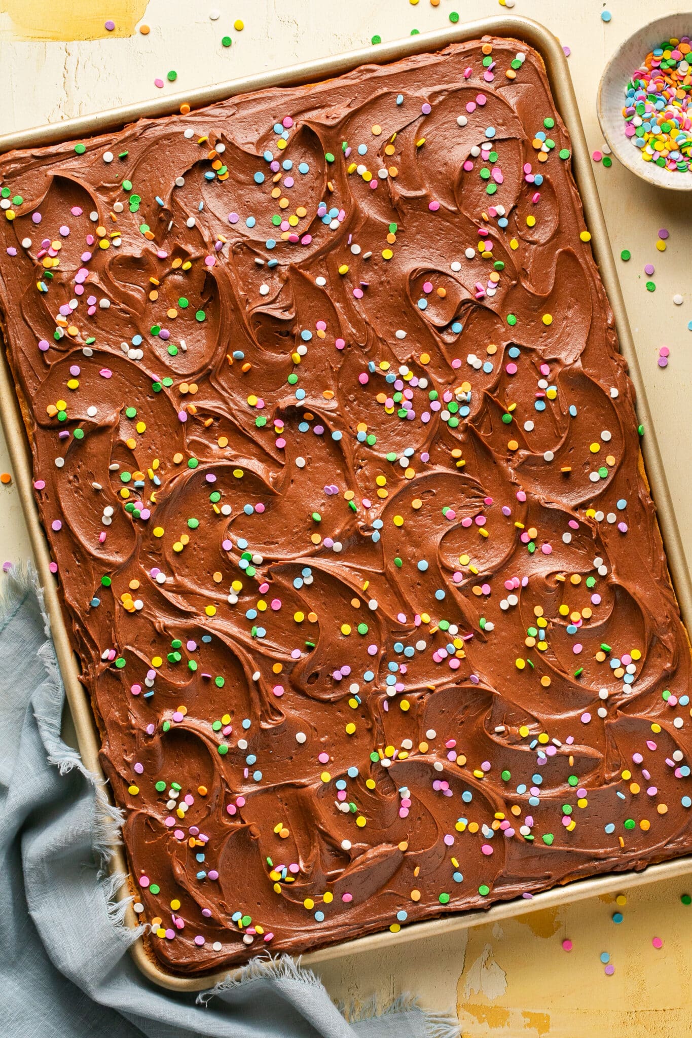 a yellow sheet cake with chocolate frosting and colorful sprinkles on top. 