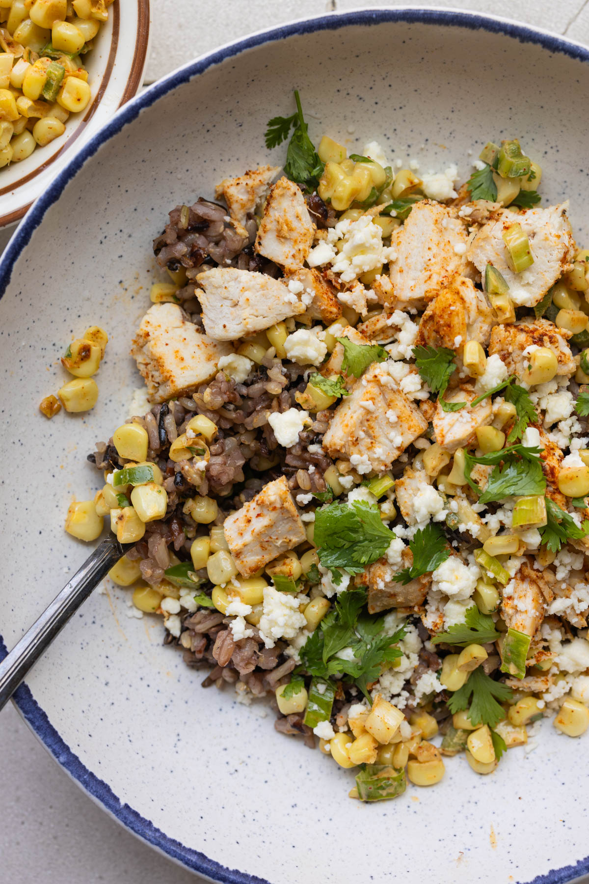 wild rice in a blue speckled and white bowl with chicken and corn and cilantro on top. 