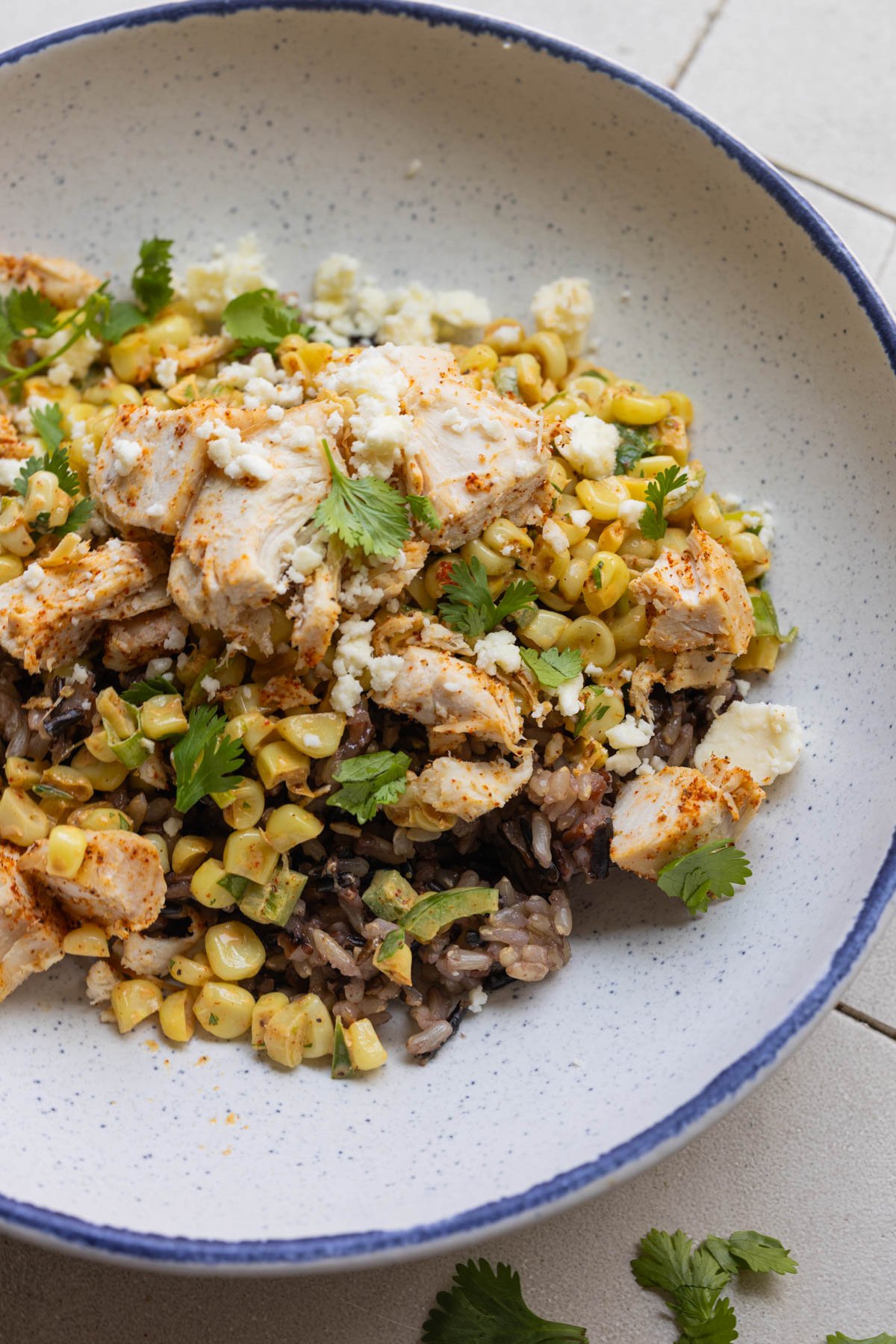 wild rice in a blue speckled and white bowl with chicken and corn and cilantro on top. 