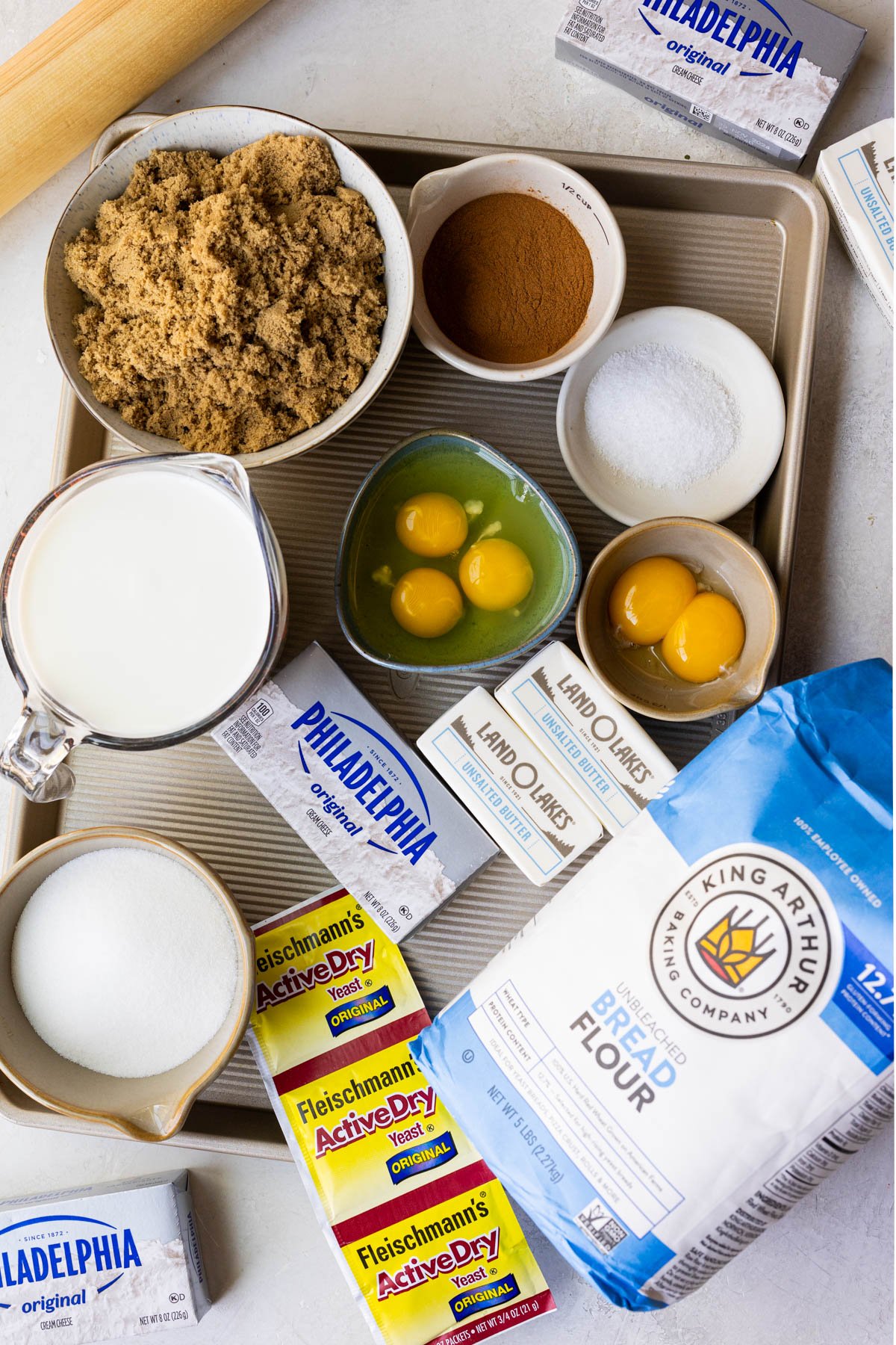 cinnamon roll ingredients in small glass dishes laid out on a gold baking sheet. 