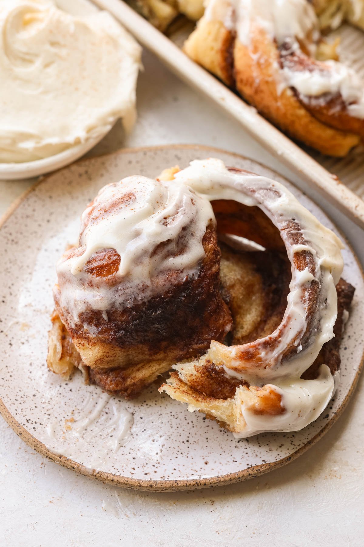 a gooey cinnamon roll on a plate with frosting on top. 