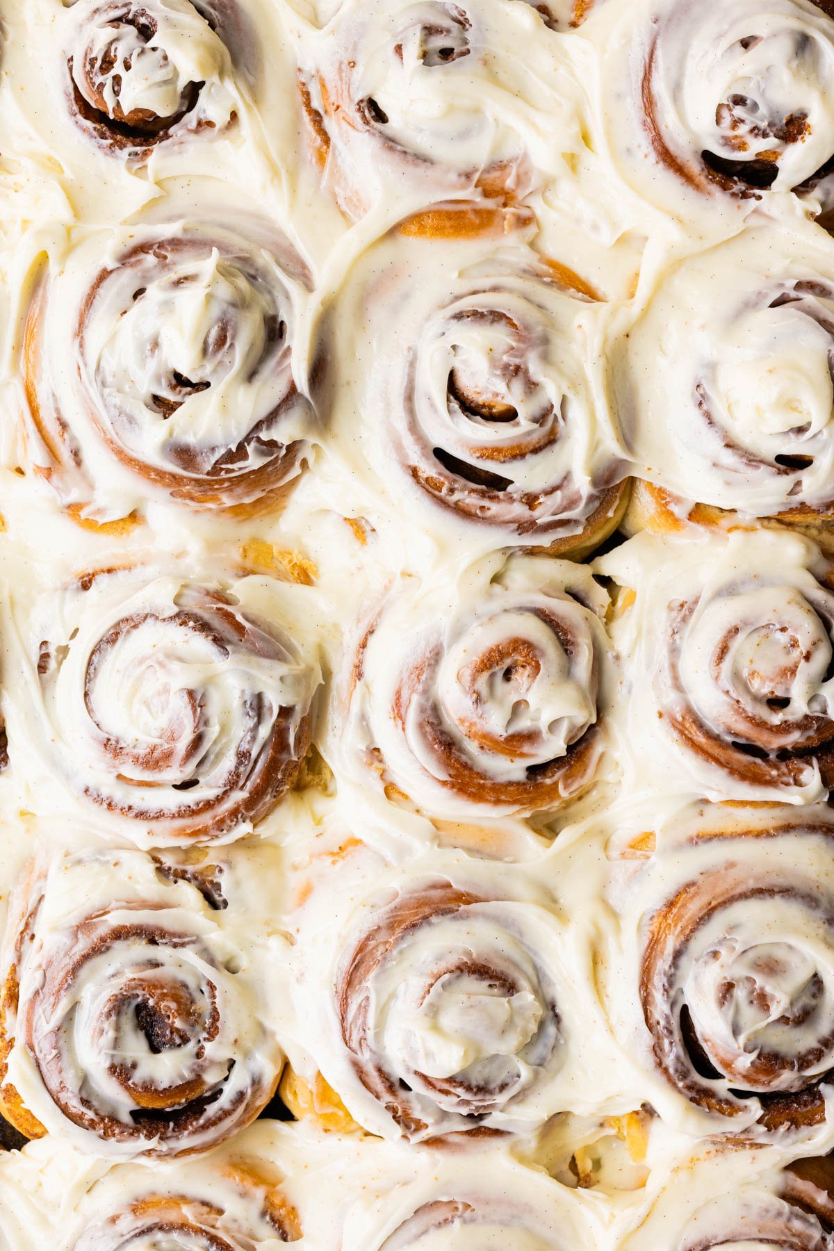 close up image of freshly baked cinnamon rolls with frosting on top. 