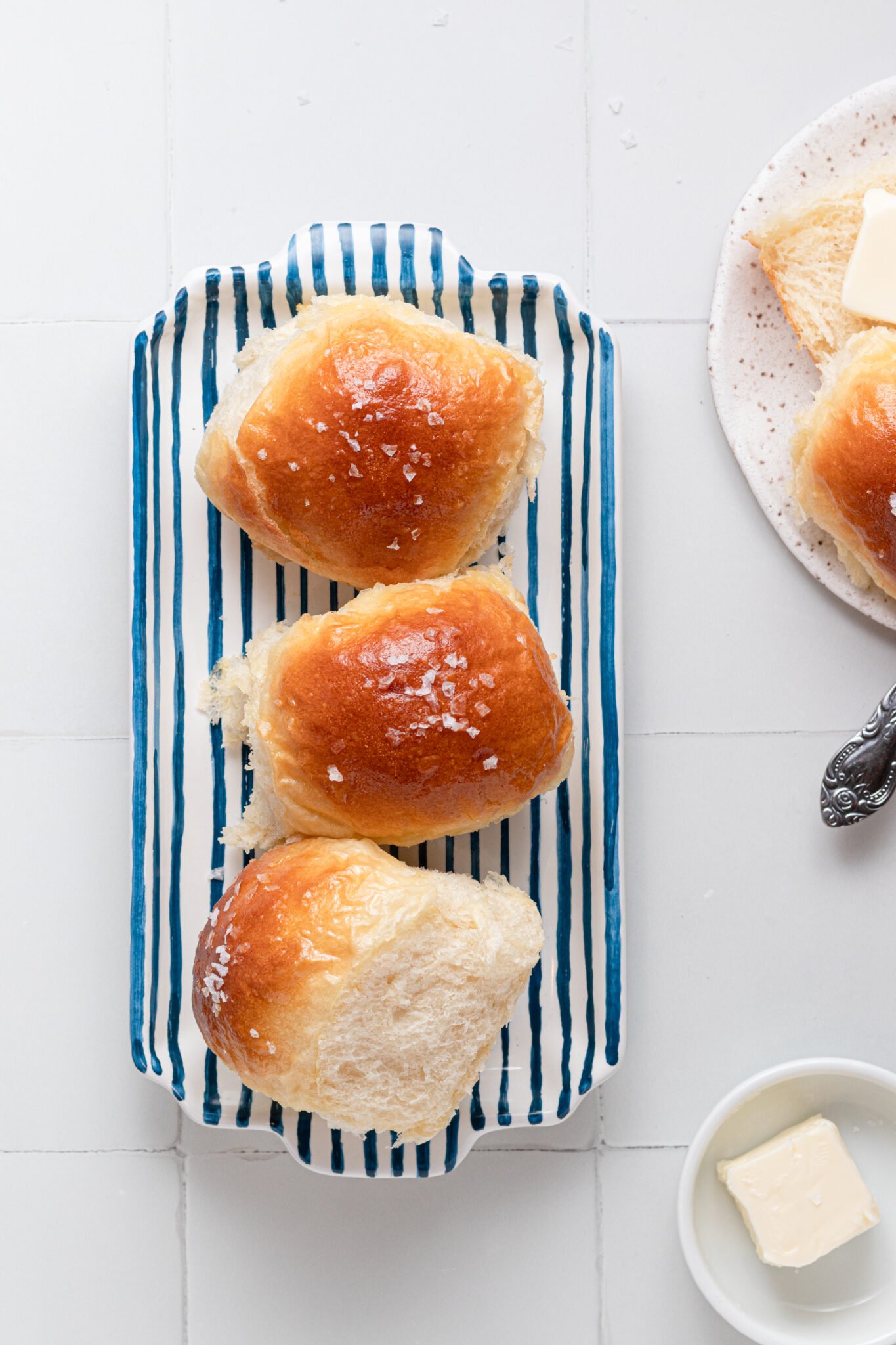 three dinner rollings on a blue striped plate with butter on the side. 