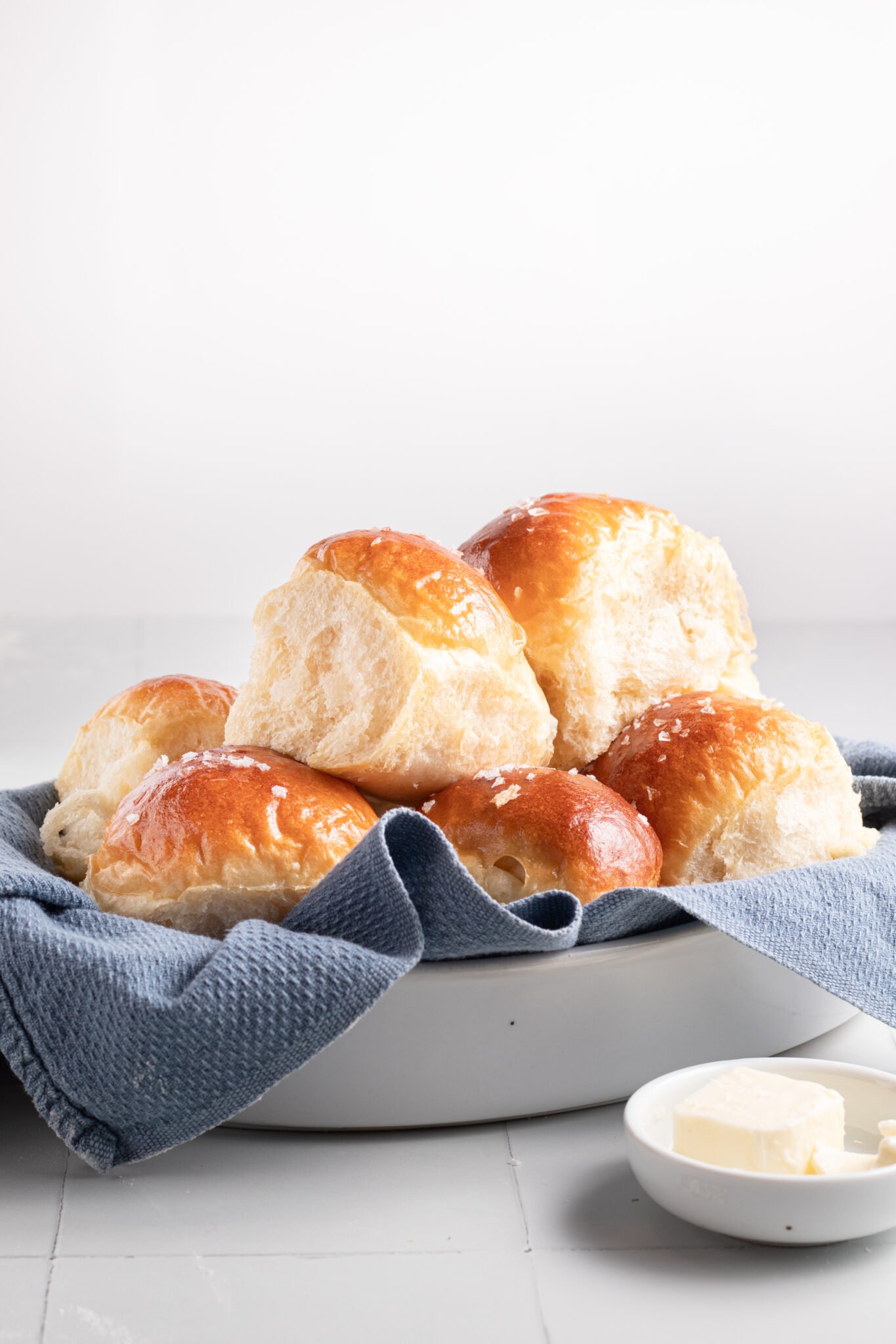 a stack of dinner rolls in a bowl with a blue towel. 