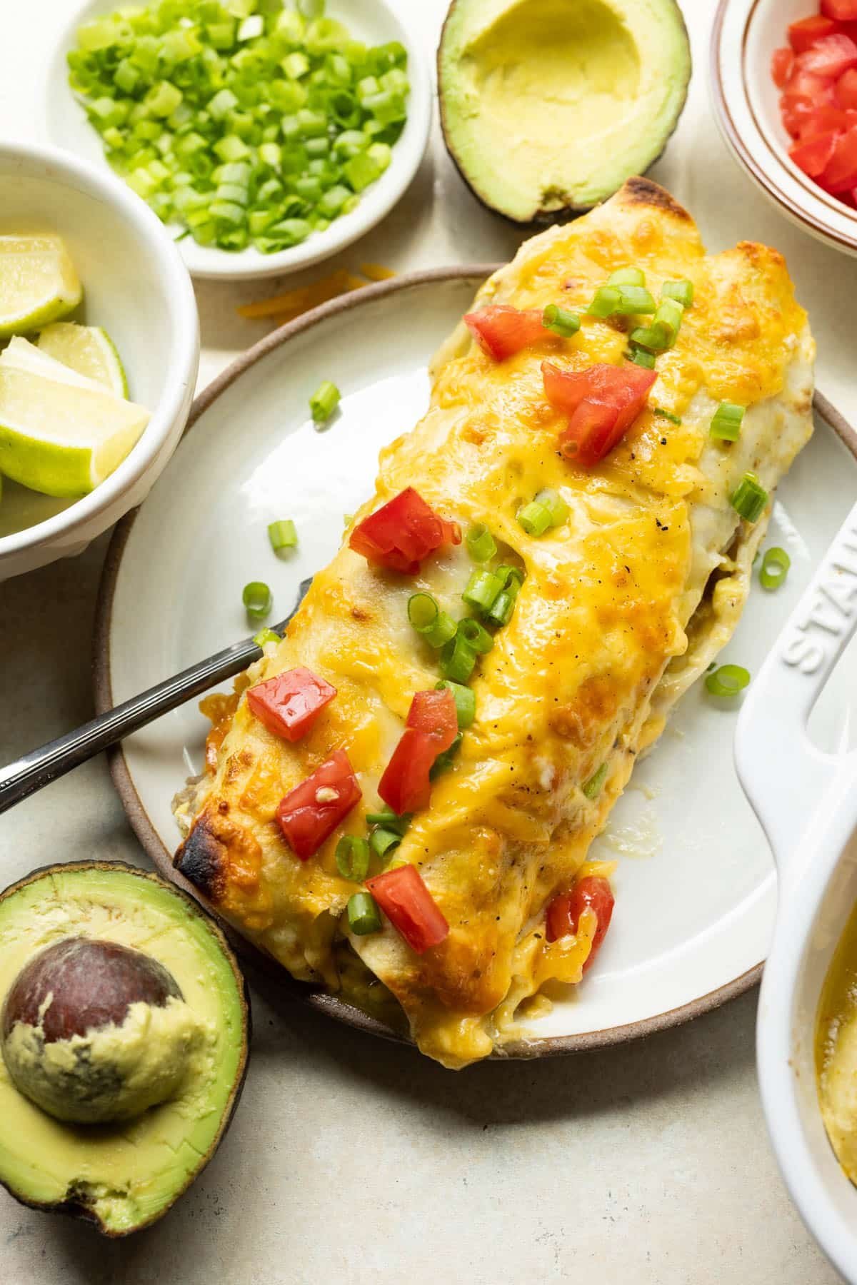 breakfast enchiladas on a white plate topped with green onions, cheese, and tomatoes. 