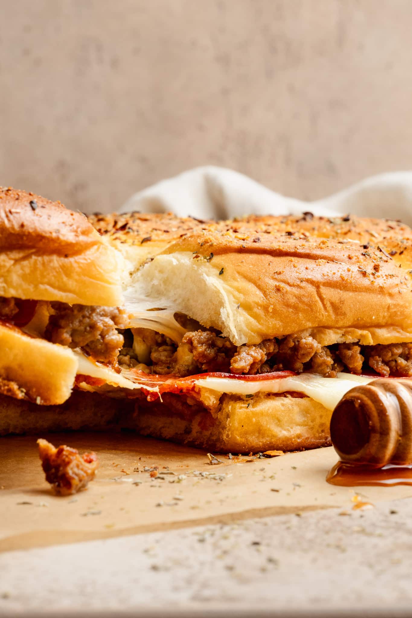 Side view of pizza sliders with one piece pulled away, revealing gooey melted cheese and savory sausage filling. The rolls are golden and glistening with garlic butter and honey.
