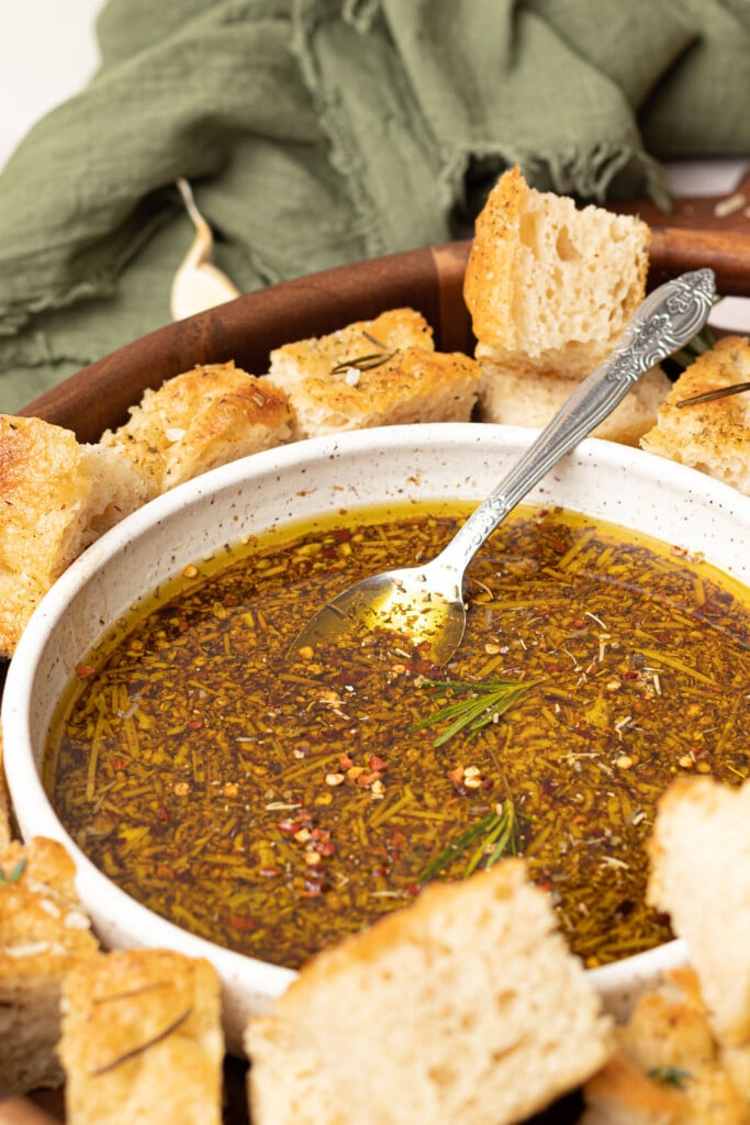 Bread dipping oil recipe in bowl with spoon and chunks of bread in serving bowl.