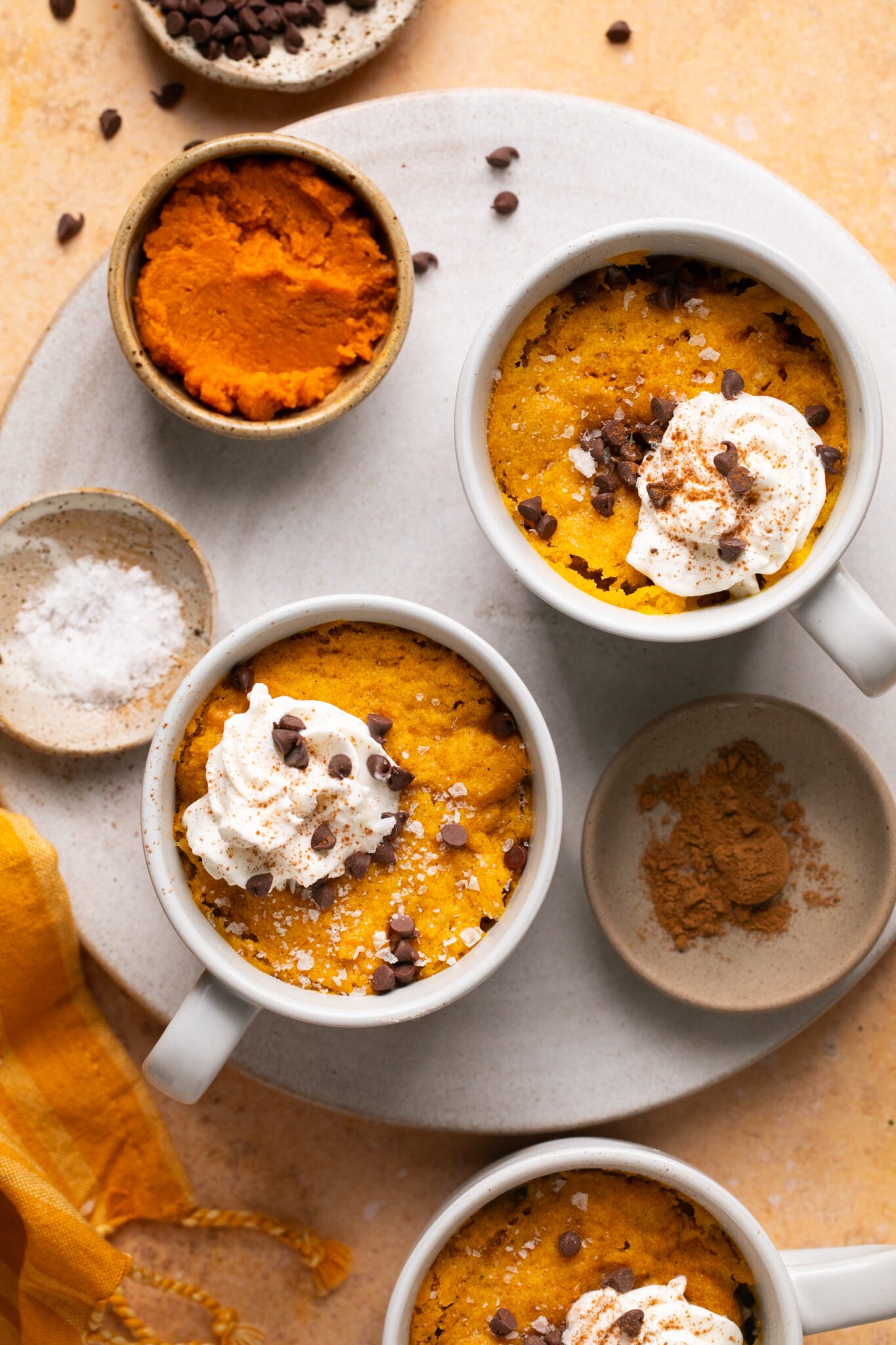 2 pumpkin mug cakes on a plate topped with whipped cream, flaky sea slat and mini chocolate chips. 