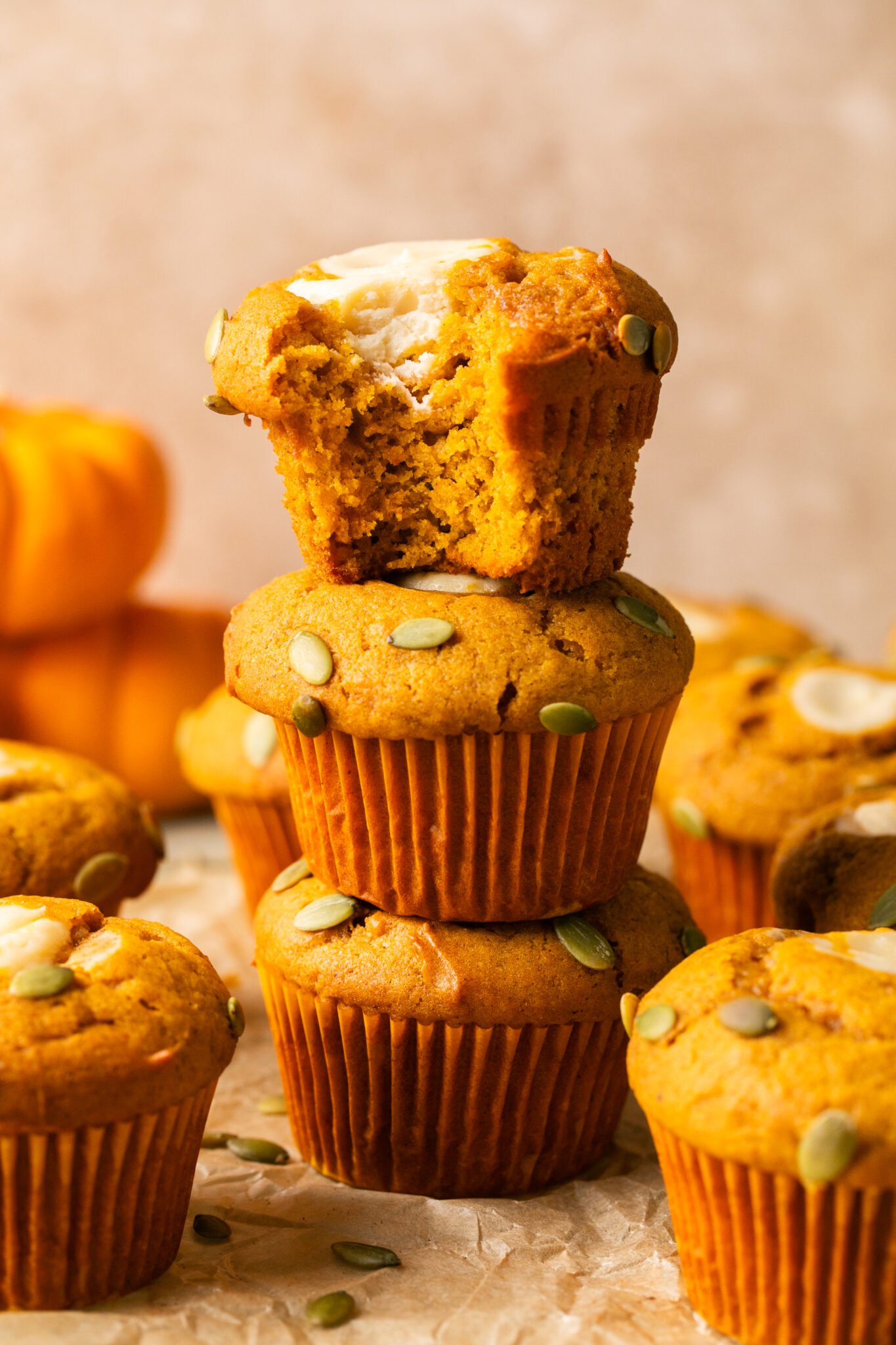 pumpkin cream cheese muffins stacked on top of each other with a bite taken out of the top pumpkin. 