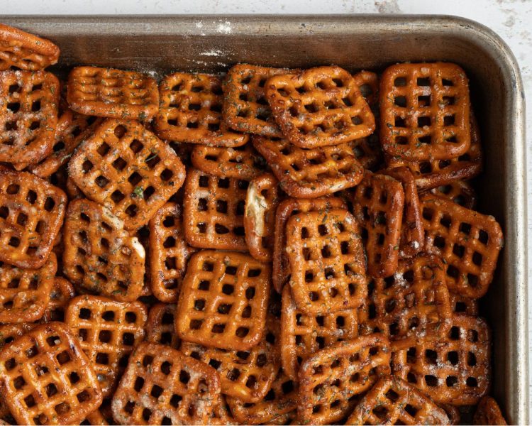 metal baking pan full of square pretzels with seasoning