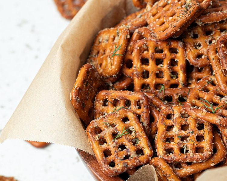 square pretzels with seasoning in a container with brown parchment paper